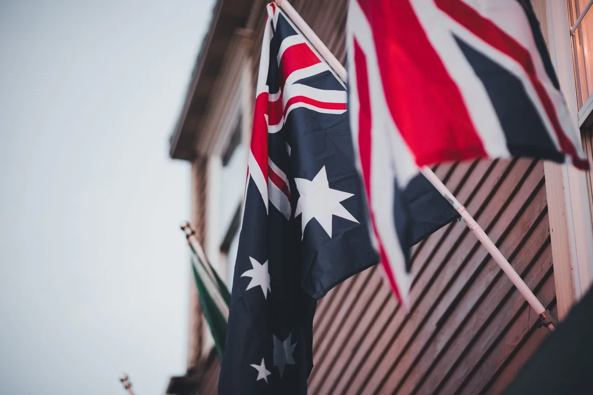 The Australian flag flying beside the Union Jack on a building exterior, comparing Australia and the United Kingdom