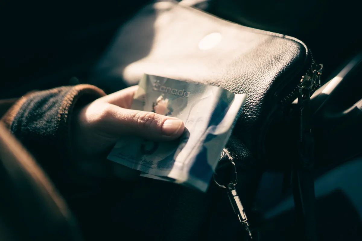 A person holding a Canadian five-dollar polymer banknote, illustrating payroll deductions in Canada