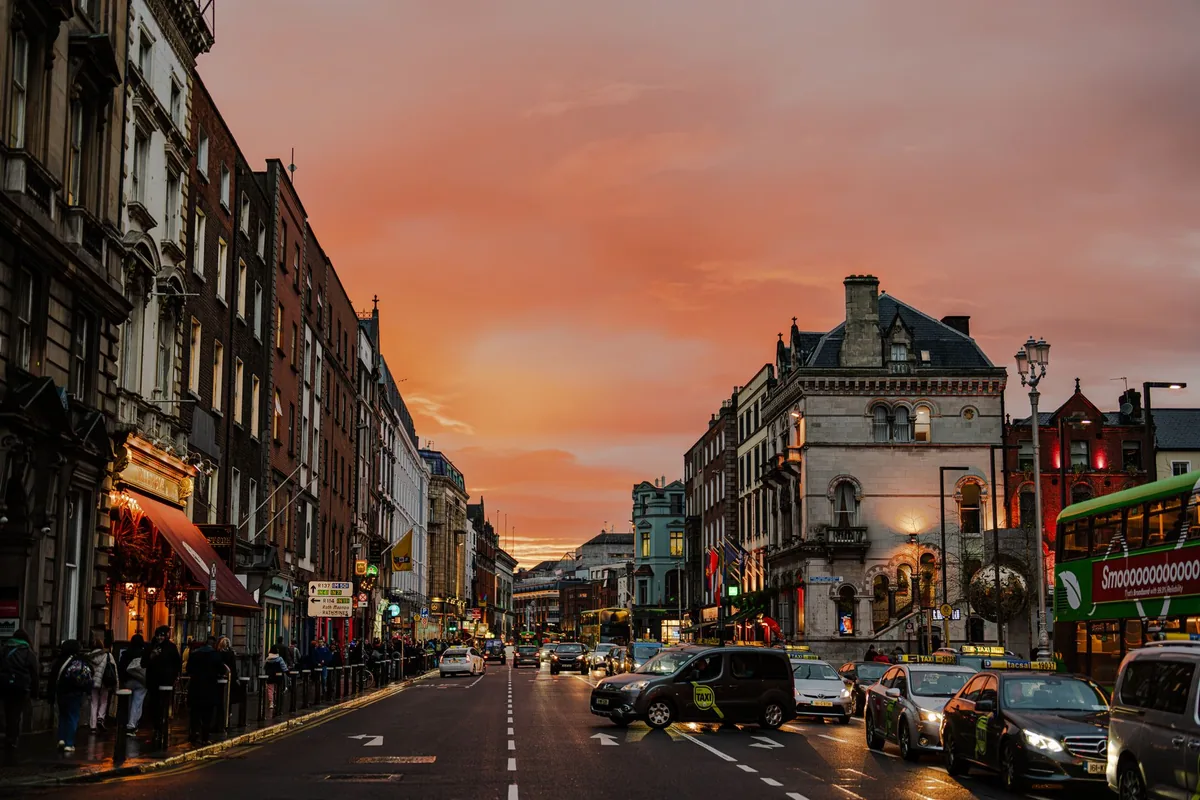 Dublin city centre street at golden sunset with red-brick buildings and traffic, illustrating Ireland vs UK take-home pay