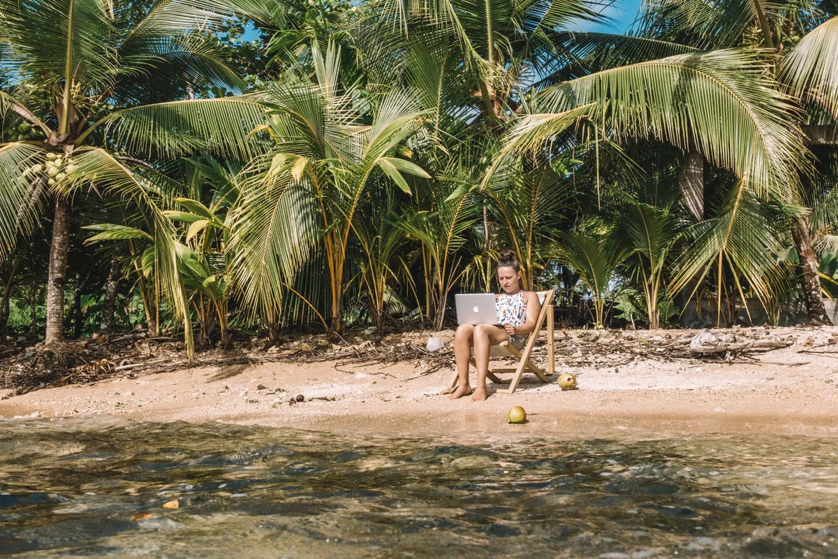 Woman working remotely on a laptop from a tropical beach, illustrating digital nomad tax obligations