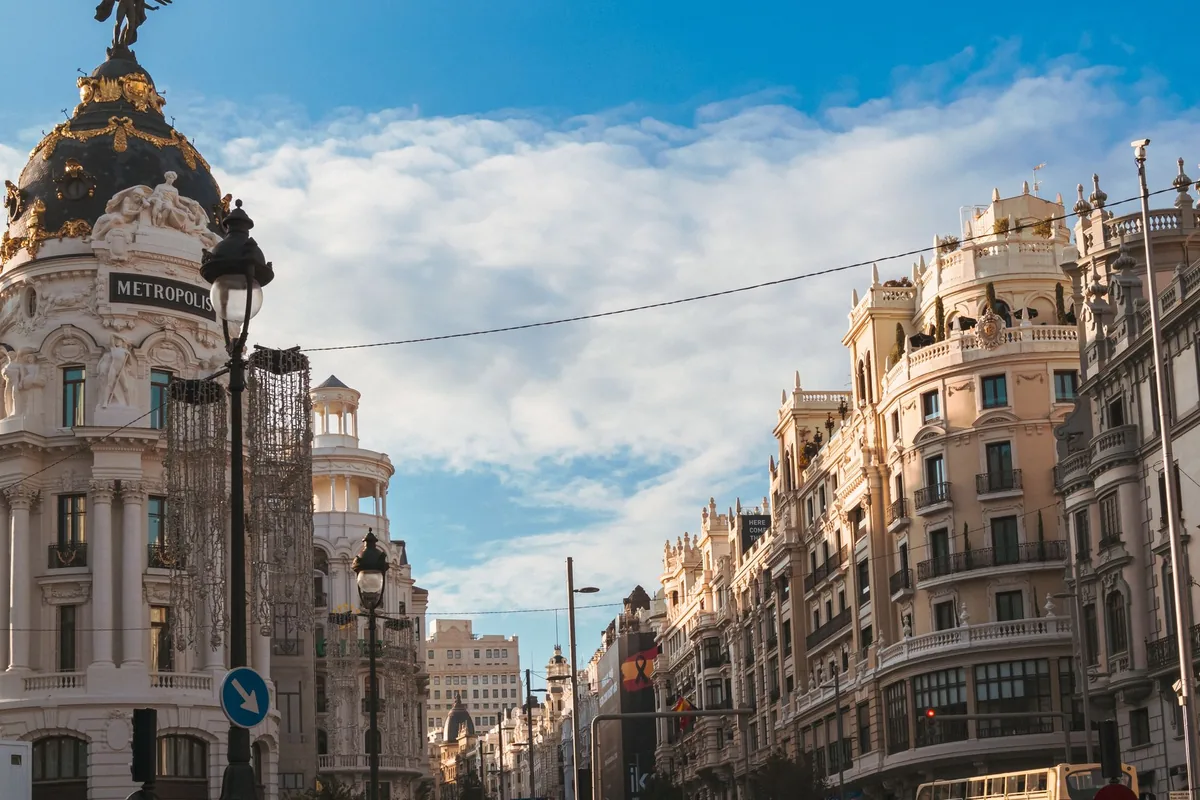 Gran Vía street in Madrid, Spain, with the Edificio Metrópolis and a Spanish flag under a clear blue sky